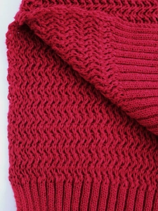 Detailed close-up of dark red knitted sweater sleeve with ribbed cuff and wavy texture