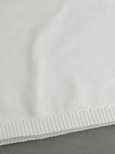 Close-up of white knitted sweater showing detailed ribbed cuff and soft fabric texture