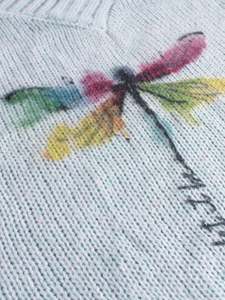 Detail of light blue knit sweater featuring colorful dragonfly pattern and ribbed V-neckline