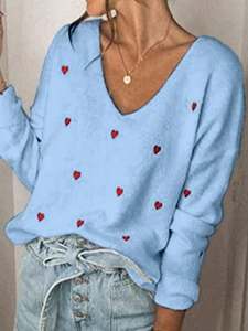Dettaglio del maglione in maglia azzurra con ricamo a cuori rossi e scollo a V classico