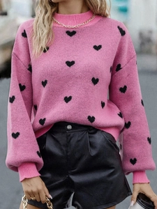 Close-up of pink rib-knit sweater featuring black heart patterns and golden chain necklace