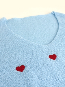 Dettaglio maglione a maglia azzurro con scollo a V e ricamo a cuore rosso