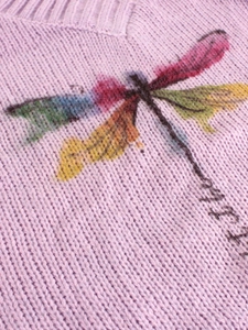 Detail of dragonfly knit pattern with colorful gradient wings on a mauve sweater