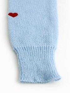 Dettaglio del polsino in maglia azzurra con cuore rosso ricamato e trama a coste