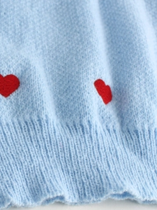 Dettaglio del maglione a maglia azzurro con cuori rossi e rifinitura a coste fine