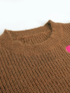 Detail of a crew neck knit sweater featuring a soft pink heart patch and fuzzy texture