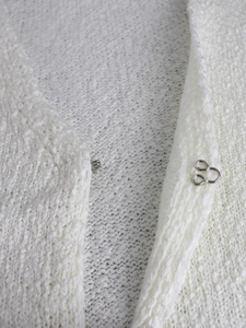 Dettaglio di un cardigan in maglia bianca con chiusura a gancio per donna