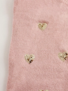 Gros plan sur un tricot rose avec un motif de cœur en paillettes dorées cousu main