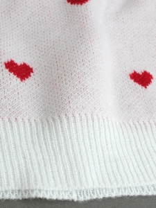 White ribbed knit sweater with red heart patterns and elastic cuffs for a romantic look