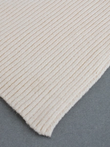 Close-up detail of cream white ribbed knit sweater fabric showing vertical texture