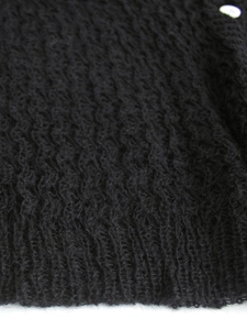 Detailaufnahme von schwarzem Strickstoff mit weißem Knopf und geripptem Bündchen am Saum