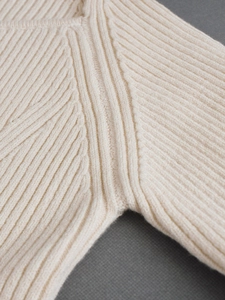 Close-up of the ribbed knit armhole seam and texture on a cream-colored sweater