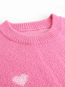 Close-up of pink knit sweater with white heart pattern and ribbed crew neck detail