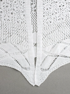 Détail de gilet blanc en maille ajourée avec motifs en dentelle pour tenue de plage chic