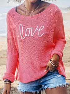 Detail of coral knit sweater with white love embroidery on the chest at beach