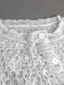 Nahaufnahme der hellgrauen flauschigen Strickjacke mit weißen Knöpfen und Lochmuster