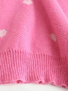 Close-up of pink knit fabric with white heart patterns and ribbed hem detail