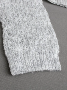 Detailansicht der hellgrauen Strickjacke mit Häkelmuster und eng anliegenden Rippbündchen