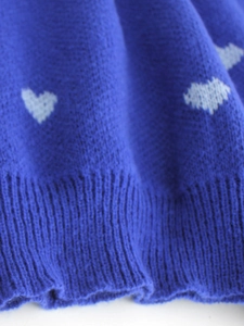 Detail of navy knit sweater showing white heart jacquard pattern and ribbed hem finish