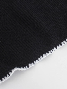 Detail of black knit vest featuring white scalloped edges and fine contrast stitching