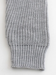 Detailed macro view of the light grey ribbed cuff and thick knit texture on the sweater