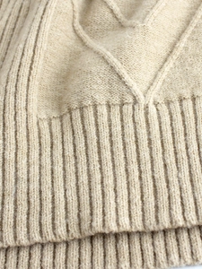 Macro shot of beige knit sweater showing detailed texture and ribbed hem craftsmanship