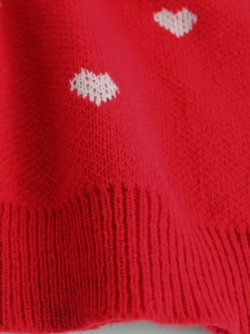 Close-up of red knit sweater with white heart pattern and ribbed hem detailing