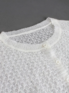 Nahaufnahme der weißen Strickjacke aus Spitze mit zartem Netzmuster und weißen Knöpfen