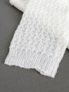 Nahaufnahme von weißem Mohair-Strickgewebe mit zartem Lochmuster und feiner Textur am Saum