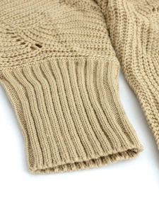 Detail of beige knit sweater showing hollow pattern textures and ribbed cuffs
