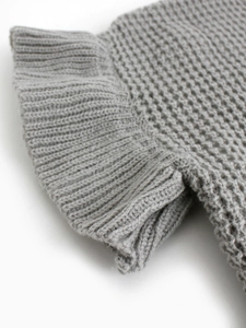 Detailed macro view of the grey knit sweater featuring delicate ruffled hem textures