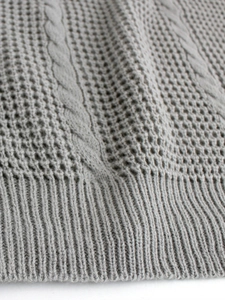Close-up of grey cable knit texture and ribbed hem detail on a short sleeve sweater
