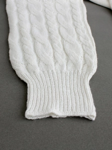 Close-up of white cable knit texture and ribbed cuff on a soft winter sweater