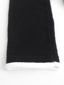 Dettaglio di manica in maglia nera con bordo arrotolato bianco e trama del tessuto