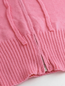Dettaglio del cardigan in maglia rosa con zip argentata e trama a costine sul fondo