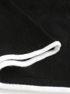Dettaglio macro dell'abito in maglia nera con bordo bianco a contrasto e texture morbida