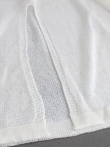 Detail shot of white lightweight knit fabric showing seam stitching and side slit texture