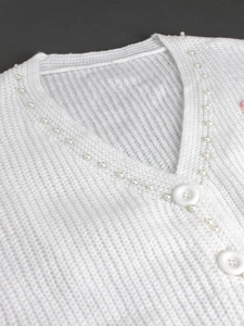 Gros plan détaillé du cardigan blanc en maille côtelée avec bordure de perles délicates