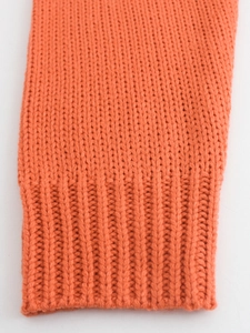 Gros plan sur la manche d'un pull en maille orange avec poignet côtelé et texture épaisse