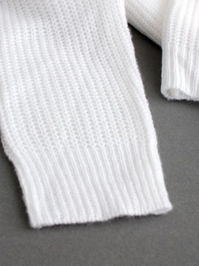 Détail macro du poignet d'un pull en tricot blanc montrant la texture et les côtes