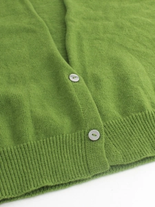 Dettaglio del cardigan in maglia verde con orlo a coste e bottoni marmorizzati
