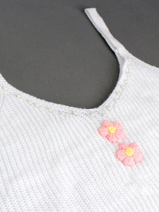 Détail d'un caraco en maille blanche avec col en V, bordure perlée et fleurs au crochet