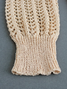 Close-up of cream knit cardigan sleeve featuring intricate crochet hollow patterns