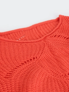 Detailed close-up of orange-red knitted sweater featuring hollow-out patterns and round neck