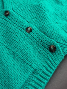 Close-up of turquoise V-neck knit cardigan with textured stitching and tortoise buttons