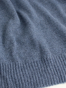 Close-up of blue knit sweater featuring ribbed hem detail and soft textured fabric