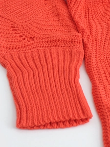 Detailed close-up of orange-red knitted sweater cuff with ribbed edge and hollow pattern
