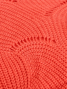 Close-up of coral red knitted sweater featuring intricate hollow wave pattern texture
