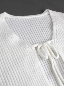 Primo piano di un cardigan bianco a costine con delicati dettagli di lacci sul collo