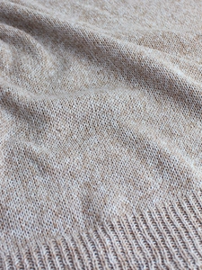 Close-up of beige knit fabric texture with ribbed hem detail for women's sweater